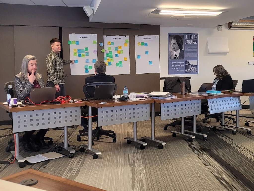 Graeme standing and pointing to a sticky note poster with three people seated