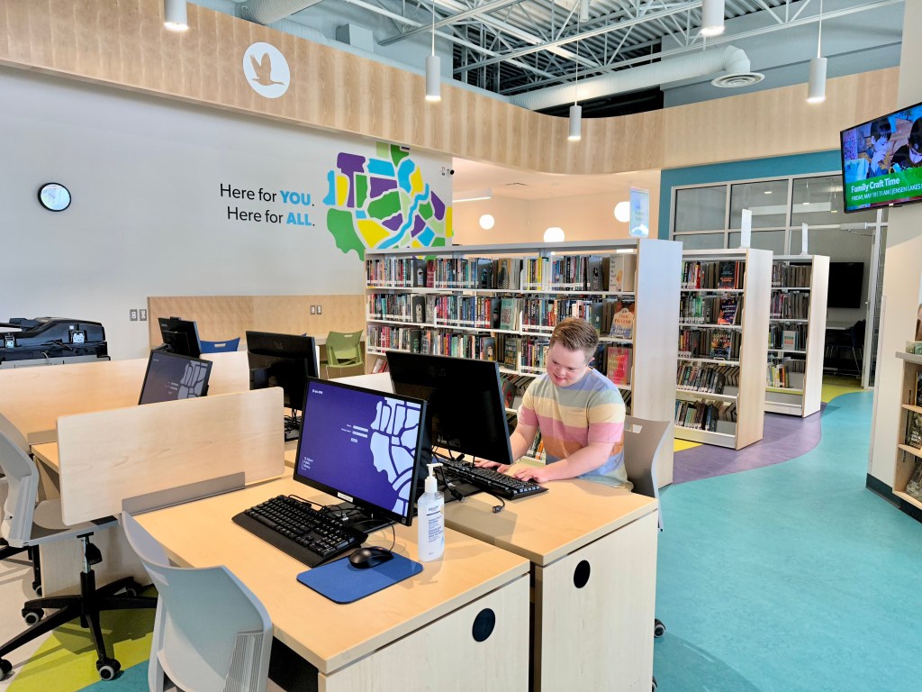 Library scene with a person working on a computer, surrounded by bookshelves