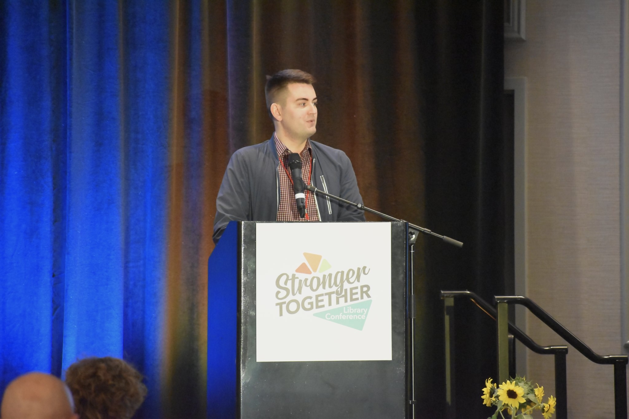 Graeme standing at a podium with a sign reading Stronger Together Library Conference